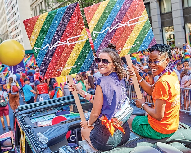 Two people celebrating pride holding rainbow MAC signs