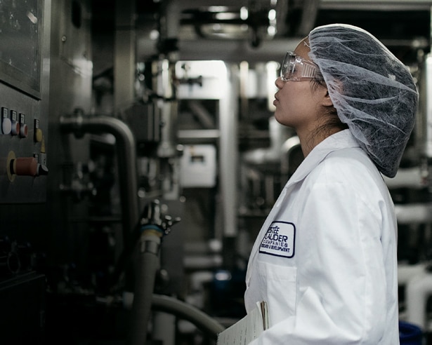 Person in factory wearing a white coat, hair net, and glasses